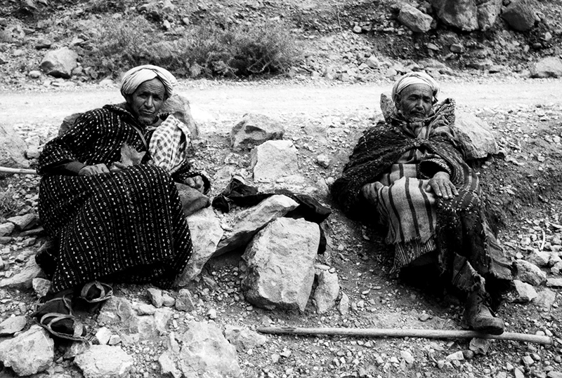 Two elderly camel herders sitting, stopped for a rest in the Sahara Desert in Algeria