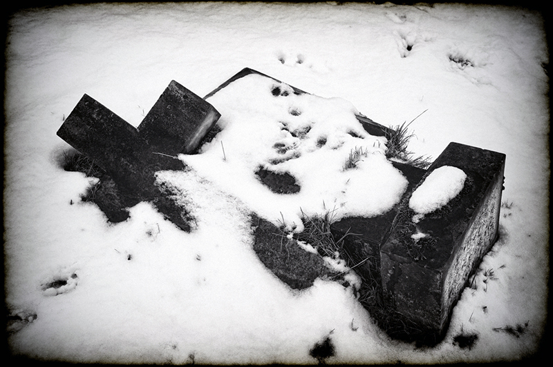 Toppled gravestone cross lying on its side covered in snow