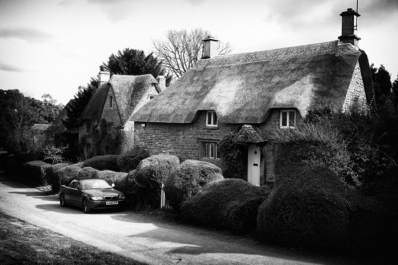 ENG0014BW15X10 BMW car sits outside a traditional thatched cottages in the Cotswold, England