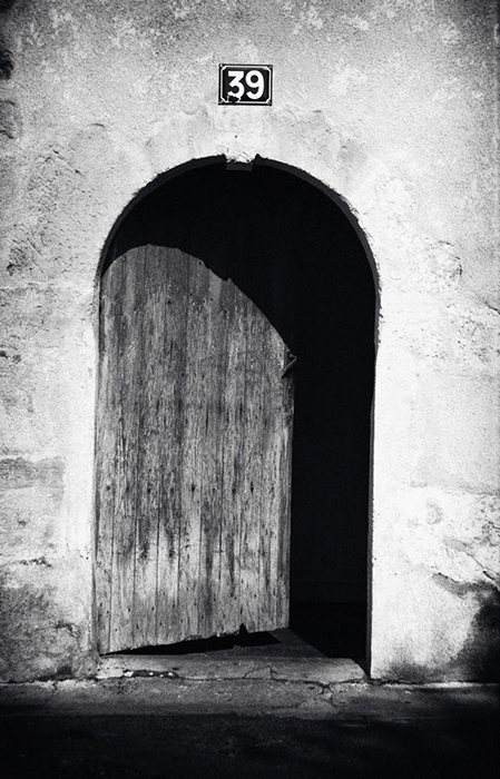 An ancient wooden door half opened with strong sunlight outside and blackness inside