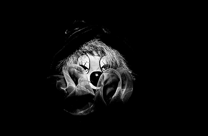 A creepy looking clown's face surrounded by black negative space