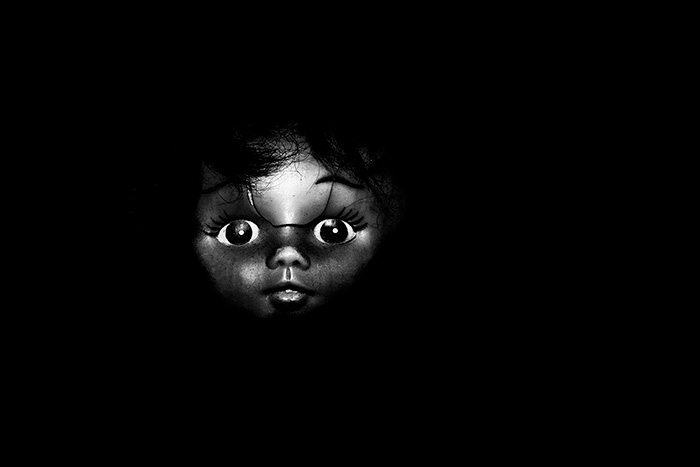 Broken doll's face with wide eyes stares out from black negative space