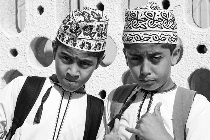 Two extroverted boys in traditional dress pose for a photograph in Oman