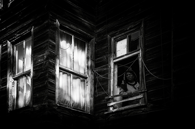 A woman peering out of her window of a traditional wooden house in an Istanbul suburb