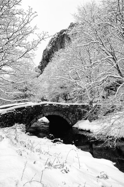 Snow covered scene with old stone bridge crossing Afon Croesor at Llanfrothen