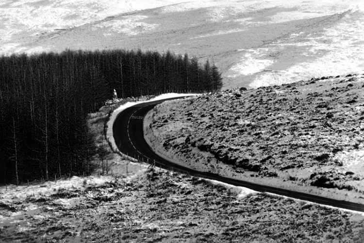 Winding Welsh road with snowy landscape and a plantation of conifers