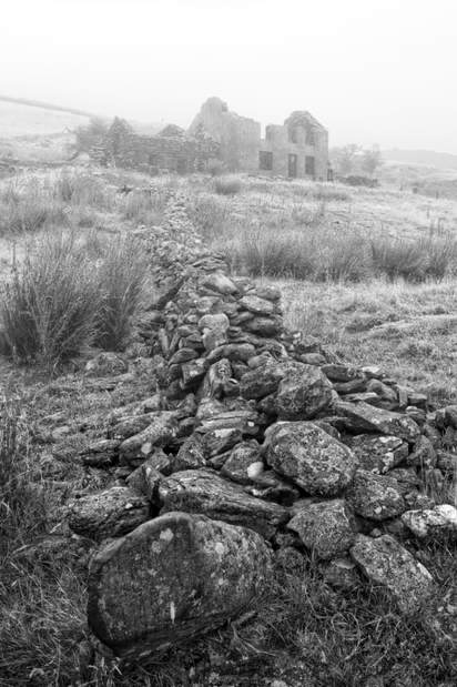 Toppled stone wall leading to a derelict house in the mist at Cwmystradllyn