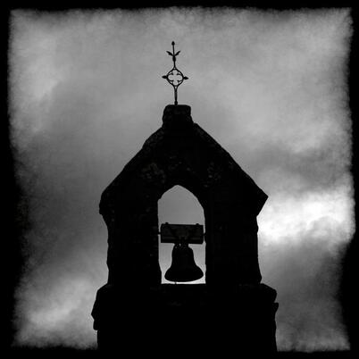Silhouette of a ancient church belfry with hanging bell with a menacing sky in the background