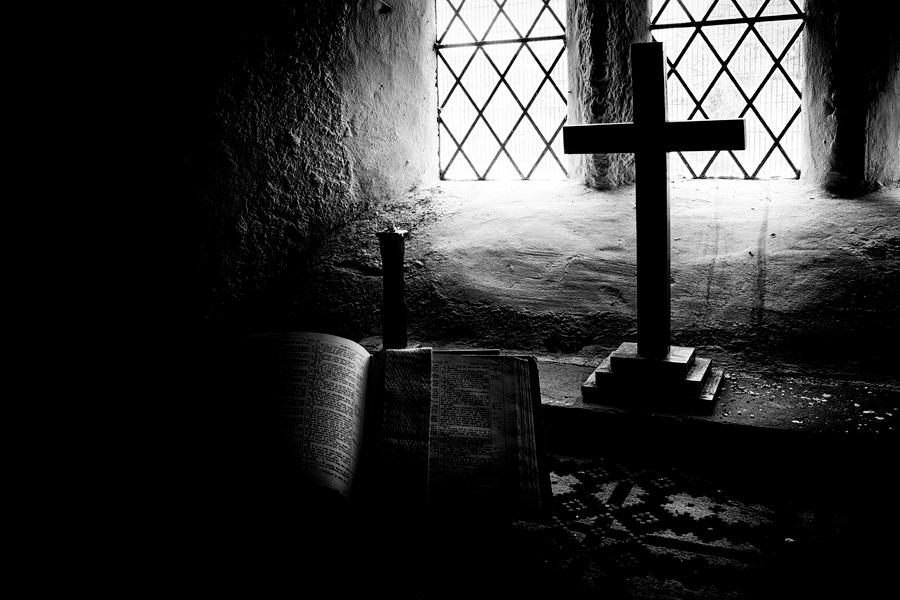 Cross and open Bible dimly lit by available light in an ancient church