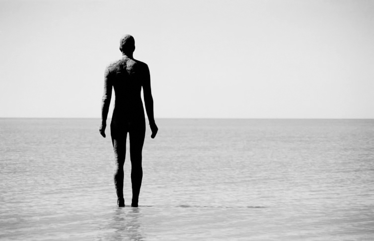Anthony Gormley statue at Crosby Beach, England photographed from behind, looking out on an empty sea