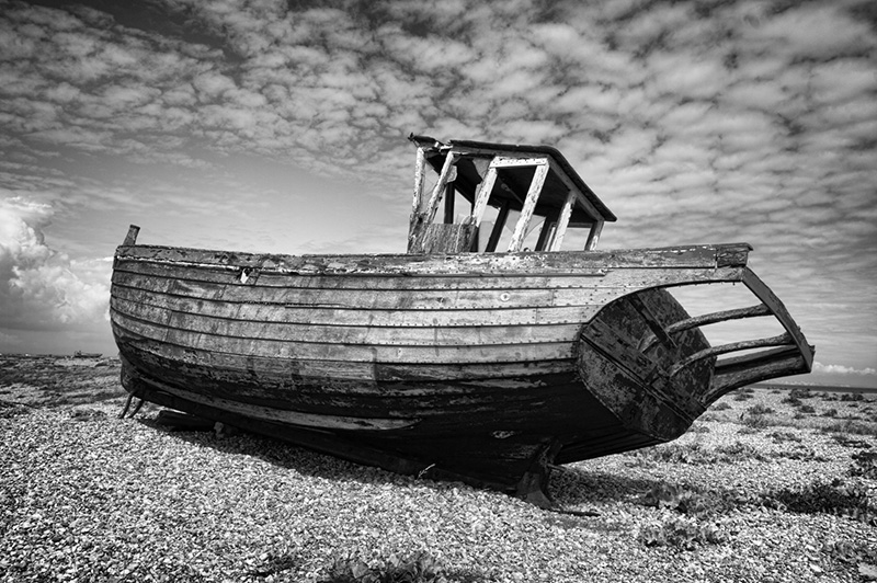 Decaying fishing boat sitting alone on the shingle beach at Dungeness