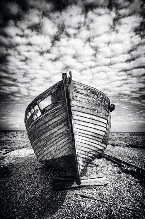 The bow of a decaying fishing boat under a mackerel sky at Dungeness