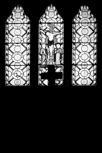 Stained glass window with Christ on a cross lit from outside light and surrounded by blackness with the silhouette of a cross in front