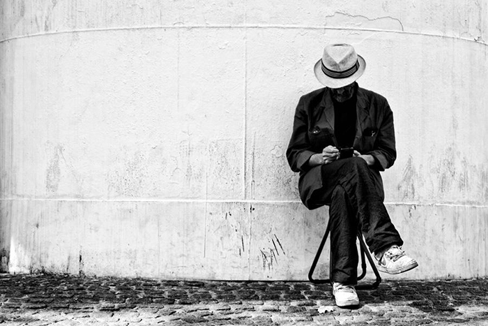 Man in hat sitting alone on a stool scrolling through his phone