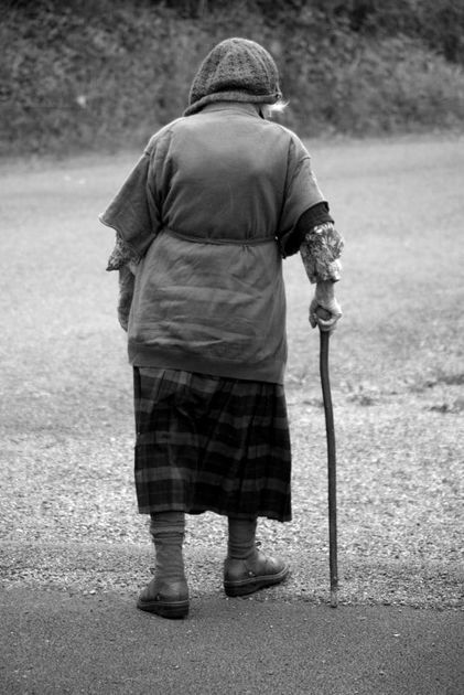 Elderly woman with a walking stick walking away from the camera