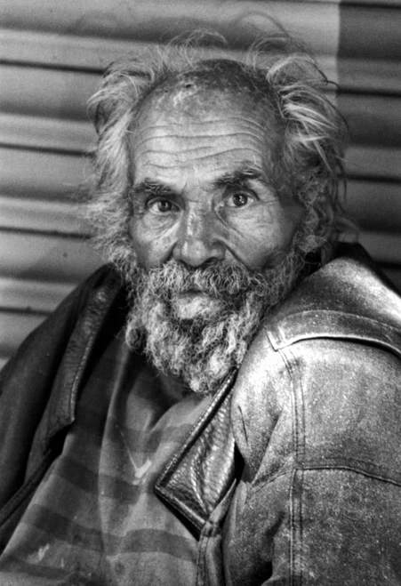 Elderly bearded homeless man in a worn leather jacket