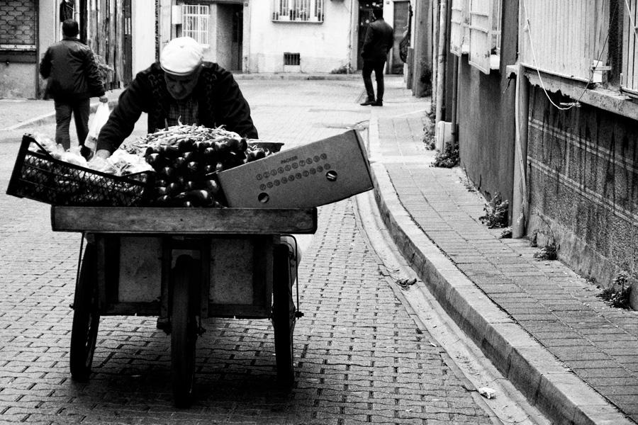 An elderly man pushes a cart full of eggplants up hill in an Istanbul suburb